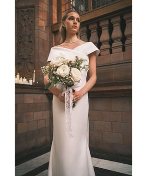 Elegant Bardot neckline with sophisticated fold-over detail for a timeless bridal silhouette
        Striking bow detail at the back adds a romantic, feminine touch
        Fishtail hem creates a dramatic, sweeping effect without the need for a traditional train
        Structured bodice with pleated waist detailing for a flattering, defined silhouette
        Short cap sleeves offer subtle coverage whilst maintaining the elegant off-shoulder design
    
    Make a striking impression on your special day with this sophisticated Bardot wedding dress from Coast. The clean lines and modern silhouette create a contemporary bridal look whilst the luxurious satin fabric catches the light beautifully as you move. The statement bow back detail adds a touch of romance to this otherwise minimalist design, whilst the fishtail hem creates a graceful sweep across the floor. Style with delicate drop earrings and a simple bracelet as seen on our model, allowing the dress to remain the focal point. For your bridal ensemble, consider a fingertip veil to complement the clean lines, or wear your hair in a sleek updo to showcase the beautiful neckline. Perfect for the modern bride seeking elegance with a contemporary twist for her wedding ceremony.