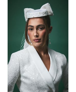Striking pillar box design with an elegant oversized bow as the centrepiece
        Delicate netting veil adds a romantic touch to this sophisticated headpiece
        Adorned with lustrous pearl embellishments for a touch of bridal luxury
        Structured silhouette sits perfectly atop the head for a statement look
        Lightweight construction ensures comfort throughout your special day
    
    Make a graceful statement on your wedding day with this exquisite bow fascinator from Coast. The architectural pillar box design creates a modern yet timeless silhouette, whilst the dramatic bow detail captures attention with its structured elegance. The delicate netting cascades beautifully, framing your face with ethereal charm. Perfect for the contemporary bride seeking a distinctive alternative to traditional veils or tiaras. Style with a sleek updo to showcase the fascinator's intricate details, or wear with softly flowing locks for a more romantic aesthetic. Pair with pearl earrings to complement the fascinator's embellishments and create a cohesive bridal ensemble that reflects sophisticated British elegance. Ideal for civil ceremonies, church weddings or as a reception accessory that transforms your look from day to evening.