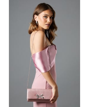 Luxurious satin clutch bag adorned with a striking diamante bow embellishment
        Elegant fold-over design with secure magnetic closure
        Detachable chain strap offering versatile carrying options
        Spacious interior with branded lining and internal pocket
        Perfect dimensions to hold all your evening essentials whilst maintaining a sleek silhouette
    
    The Galaxy Satin Diamante Bow Brooch Clutch Bag from Coast is the quintessential finishing touch for your most memorable occasions. The eye-catching diamante bow creates a focal point that captures the light beautifully as you move, whilst the smooth satin exterior conveys refined sophistication. Style with a tailored jumpsuit as shown, or pair with a flowing evening gown for black-tie events. The versatile chain strap allows you to transition effortlessly from clutch to shoulder bag when mingling at cocktail receptions or attending formal dinners. This clutch is particularly well-suited for wedding celebrations, race day outings, or any event where elegance is paramount. A true investment piece that will complement your occasion wardrobe for seasons to come.