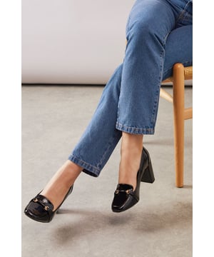 Wide fit design offers exceptional comfort for all-day wear
        Striking faux patent leather finish adds a sophisticated sheen
        Decorative metal hardware detail on the front creates visual interest
        Sturdy block heel measures between 7-9cm for confident height
        Classic loafer silhouette with contemporary proportions for versatile styling
    
    These Lucky loafers from Wallis present the perfect marriage of comfort and sophistication for your workwear wardrobe. The wide fit construction ensures these high block heels remain comfortable throughout your busy day, whilst the glossy patent finish lends a polished touch to any ensemble. Style them with tailored trousers as shown for a refined office look, or pair with a pencil skirt and crisp blouse for important meetings. The substantial block heel provides stability without sacrificing elegance, making these an excellent choice for long days at the office. For after-work occasions, these versatile loafers transition beautifully to evening drinks or dinner engagements when paired with smart denim and a structured blazer. A truly indispensable addition to the sophisticated woman's footwear collection.