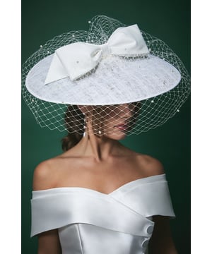 Striking wide brim fascinator with delicate pearl-adorned veil for a romantic finish
        Statement bow detail adds a contemporary touch to this classic bridal accessory
        Textured fabric base provides structure and sophistication
        Lightweight design ensures comfort throughout your special day
        Secures easily with discreet attachments for worry-free wear
    
    Make a captivating entrance on your wedding day with this exquisite Lisa Tan bridal fascinator from Coast. The wide brim silhouette creates a dramatic yet elegant profile, whilst the delicate veil adorned with subtle pearls adds a touch of romance and tradition. The statement bow detail introduces a modern twist to this timeless accessory, perfectly complementing an off-shoulder wedding gown as shown. This versatile piece works beautifully with both classic updos and flowing locks, allowing you to create your desired bridal aesthetic. Beyond the ceremony, this fascinator transitions seamlessly to the reception, maintaining its graceful presence throughout your celebrations. Pair with minimal jewellery to let this showstopping headpiece command attention, or match with pearl accessories for a coordinated bridal ensemble that reflects sophisticated British wedding style.