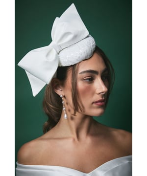 Elegant pillbox fascinator featuring a statement oversized bow detail
        Delicate lace detailing with subtle sequin embellishment for a touch of sparkle
        Secure headband design ensures comfortable wear throughout your special day
        Handcrafted from lightweight Abaca material for all-day comfort
        Versatile positioning allows for personalised styling to complement your bridal look
    
    Make a sophisticated statement on your wedding day with this exquisite Lisa Tan bridal fascinator. The classic pillbox silhouette is beautifully modernised with an eye-catching bow that adds dramatic flair without overwhelming your bridal ensemble. The intricate lace detailing creates a textural contrast against the smooth bow, offering a perfect balance of traditional craftsmanship and contemporary design. Style with an off-shoulder wedding gown as shown for a harmonious bridal aesthetic, or pair with a sleek updo to showcase dangling earrings for added glamour. This fascinator works beautifully with both classic and modern bridal styles, offering the perfect finishing touch whether you're walking down the aisle, posing for photographs, or celebrating at your reception. The secure fit ensures you can dance the night away with confidence.