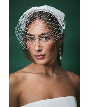 Elegant satin bow headband with delicate pearl-adorned veiling for a timeless bridal look
        Sophisticated birdcage veil design that frames the face beautifully
        Versatile one-size fit suitable for various hairstyles
        Intricate netting detail with subtle pearl embellishments throughout
        Structured bow accent that adds a touch of classic romance
    
    The Lisa Tan Bridal Bow Headband combines vintage charm with contemporary elegance, making it the perfect finishing touch for your wedding day ensemble. The delicate pearl-adorned veiling creates a soft, romantic frame for your face whilst the structured satin bow adds a touch of refined sophistication. This versatile headpiece complements both traditional and modern bridal styles, working beautifully with updos, loose waves, or sleek straight hair. Pair with simple drop earrings as shown for a coordinated look that won't overwhelm your bridal attire. The birdcage veil element offers a hint of mystery and allure, whilst still allowing your makeup to shine through. This headpiece strikes the perfect balance between statement and subtlety, ensuring you feel every bit the elegant bride on your special day.