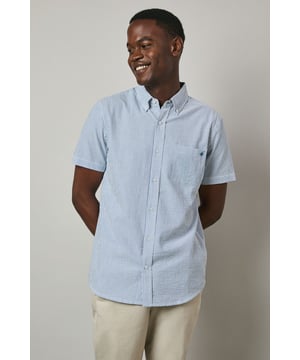 Classic button-down collar with signature Maine embroidered logo detail
        Textured seersucker stripe pattern adds visual interest and dimension
        Short sleeves with neat hems for warm-weather comfort
        Practical chest pocket for added functionality
        Back pleat detail allows for enhanced movement and comfort
    
    This Maine seersucker stripe shirt combines timeless style with practical comfort for the warmer months. The distinctive textured fabric creates a naturally relaxed look that requires minimal ironing-perfect for both holiday packing and everyday wear. As shown, pair with neutral chinos and white trainers for an effortlessly smart-casual ensemble that works brilliantly for weekend brunches or garden gatherings. The versatile design transitions seamlessly from daytime casual to evening drinks-simply tuck in and add a lightweight blazer for more formal occasions. The breathable woven fabric makes this shirt an ideal choice for summer events where you want to maintain a polished appearance without compromising on comfort.
