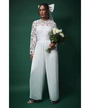 Exquisite lace bodice with intricate detailing and long sleeves
        Elegant crew neckline complemented by delicate lace overlay
        Defined waistband creating a flattering silhouette
        Dramatic pleated wide-leg trousers for graceful movement
        Statement bow detail at back for a memorable bridal finish
    
    Make a striking impression on your special day with this sophisticated jumpsuit from Coast. The beautifully crafted lace top features intricate detailing that adds a touch of romance, whilst the pleated wide-leg trousers create a dramatic silhouette that flows gracefully as you move. The defined waistband accentuates your figure, creating an elegant hourglass shape. Style with minimal jewellery to let the jumpsuit's details shine - delicate drop earrings as shown complement the look perfectly. Complete your bridal ensemble with strappy heeled sandals and a simple bouquet for a contemporary alternative to the traditional gown. This stunning piece offers both comfort and style for your wedding ceremony, allowing you to dance the night away whilst maintaining an effortlessly chic appearance.