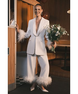 Luxurious tuxedo-style blazer with dramatic feather trim detailing at the cuffs
        Elegant shawl collar design creates a sophisticated neckline
        Single-breasted fastening with subtle button closure for a clean silhouette
        Tailored fit with gentle waist definition for a flattering shape
        Versatile styling piece that works beautifully as bridal outerwear or statement evening attire
    
    Make a striking entrance on your special day with this show-stopping Coast tuxedo blazer. The sumptuous satin fabric creates a lustrous finish while the statement feather trim adds theatrical flair to this contemporary bridal piece. The clean lines of the shawl collar and single-breasted design offer a modern take on classic tailoring, perfect for the fashion-forward bride. Style with the matching feather-trimmed trousers as seen for a complete bridal power suit, or layer over a sleek column dress for your evening reception. Complete the look with statement drop earrings and elegant heeled sandals for a bridal ensemble that beautifully balances tradition with high-fashion sensibility. This versatile piece transitions effortlessly to other special occasions beyond your wedding day.