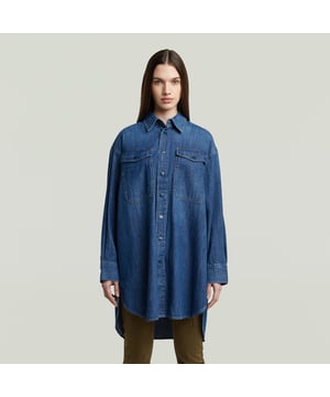 Shirt collar. Snap button closure. Flap pockets at the chest, snap buttons. Cuffs, snap buttons. Shoulder panel. Snap button. This Evergreen shirt is inspired by a Western denim shirt. It is designed in an oversized fit and reaches the upper leg. The sides are cut rounded and offer slits. Aside flap pockets at the chest, this denim shirt also offers a shoulder panel with a volume pleat underneath. 100% Cotton. Rigid. LOOSE