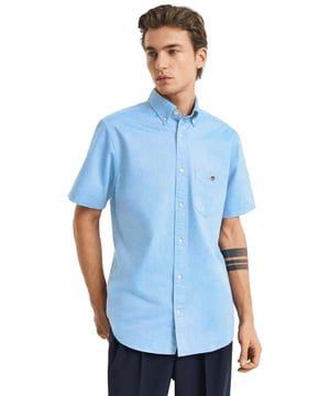 Clásica y versátil, la camisa Oxford es una prenda esencial de estilo smart-casual confeccionada en algodón resistente. Diseñada con corte regular y mangas cortas, es perfecta para los meses más cálidos. Sus detalles incluyen un cuello abotonado, bajo curvado, bolsillo en el pecho con bordado de escudo y una tabla en la espalda con presilla para mayor comodidad y estilo.