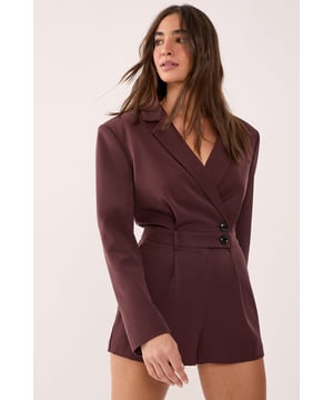 Tailored romper featuring a sophisticated wrap-style front with button detail closure
        Structured blazer-inspired lapel collar adds a smart, professional edge
        Long sleeves with subtle button cuffs for refined detailing
        Defined waistline creates a flattering silhouette
        Fully lined for comfort and smooth wear
    
    Make a statement in this striking tailored romper that seamlessly blends sophistication with contemporary style. The blazer-inspired design with its structured lapels and wrap-front detail creates a polished look that commands attention. Perfect for smart casual events where you want to showcase your fashion-forward sensibilities whilst maintaining an air of refinement. Style with knee-high boots for an evening out, or dress it down with chunky trainers for a modern daytime ensemble. For more formal occasions, pair with strappy heels and statement jewellery to enhance its elegant appeal. The versatile design transitions effortlessly from office to evening drinks, making it an essential addition to your wardrobe. This NastyGal piece offers the perfect balance of comfort and style for the fashion-conscious woman who isn't afraid to stand out.