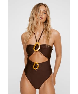Striking bandeau swimsuit featuring distinctive abstract ring cut-outs at both the bust and midriff
        Halterneck design with elegant ties that provide adjustable support and comfort
        Statement decorative rings in contrasting hue add artistic flair and visual interest
        Flattering cut-out detail creates a sophisticated peek-a-boo effect between bust and waist
        High-leg cut elongates the silhouette for a leg-lengthening effect
    
    Make a bold statement poolside with this eye-catching NastyGal swimsuit that combines contemporary design with flattering form. The innovative abstract ring details create a striking focal point whilst the bandeau style offers a clean, modern aesthetic. Perfect for those who appreciate distinctive swimwear, this piece transitions effortlessly from lazy days by the pool to beach club socials. Style with oversized sunglasses and a flowing kimono for casual poolside lounging, or pair with a sheer sarong and metallic sandals for sunset beach parties. The halterneck design ensures comfortable support for swimming and sunbathing alike, whilst the cut-out detail adds a touch of allure that will turn heads at any holiday destination. This swimsuit embodies confidence and contemporary style for the fashion-forward beach-goer.