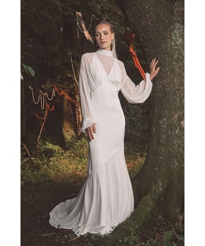 Ethereal chiffon overlay creates a romantic bohemian silhouette
        Elegant high neckline with sheer panel adds sophisticated allure
        Dramatic billowing long sleeves for a graceful statement
        Flowing maxi length with gentle train for a regal entrance
        Wrap-style bodice with tie detail accentuates the waistline
    
    This enchanting Coast wedding dress captures bohemian elegance with its flowing chiffon overlay and graceful silhouette. The sophisticated high neckline features a sheer panel that adds a contemporary touch to the traditional bridal aesthetic, whilst the billowing long sleeves create a dramatic yet delicate effect. The wrap-style bodice cinches beautifully at the waist, flowing into a sweeping maxi length that moves effortlessly with every step down the aisle. Style with minimal jewellery, as seen with the model's subtle drop earrings, to maintain the dress's ethereal quality. Perfect for garden ceremonies, countryside celebrations or intimate beach weddings, this gown offers the modern bride a blend of timeless romance and free-spirited charm that photographs beautifully in natural light.