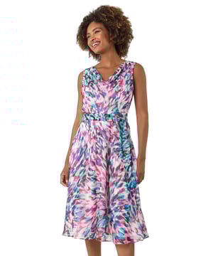 Abstract Print Chiffon Cowl Neck Dress from Roman. Add a touch of elegance to your wardrobe with this stunning abstract print dress. The comfortable chiffon fabric and sleeveless design make it perfect for warmer days, while the tie belt cinches in the waist for a flattering fit. The knee-length hem and eye-catching print ensure you stand out in style. Pair with strappy heels and a trendy bolero for a polished and sophisticated look!