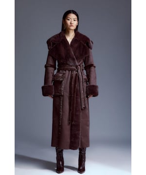 Elevate your cold-weather wardrobe with this magnificent coat, an ode to timeless luxury. Draped in premium shearling fabric, this coat exudes opulence. This outerwear piece features a maxi length and a wrap belt that gracefully cinches the waist. Style with a roll-neck jumper and knee-high leather boots for a sophisticated ensemble.Soft Shearling FabricTie BeltNotched collarLongline length