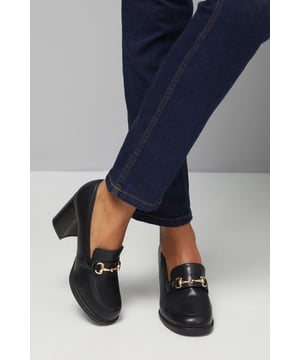Elegant wide fit loafers featuring a sophisticated gold-tone snaffle trim detail
        Comfortable high block heel measuring between 7-9cm for all-day wearability
        Crafted with a genuine leather upper for durability and quality
        Classic square toe design offering extra room for comfort
        Versatile slip-on style with a cushioned insole for additional support
    
    These Wallis Daffie loafers combine timeless sophistication with modern comfort, perfect for the woman who doesn't compromise on style or wearability. The distinctive snaffle trim adds a touch of glamour to these otherwise classic loafers, whilst the substantial block heel provides stability and height. Pair with tailored trousers and a crisp blouse for a refined office ensemble, or style with straight-leg jeans and a structured blazer for smart-casual meetings. The wide fit design ensures comfort throughout your busy day, from morning presentations to evening networking events. These versatile shoes transition seamlessly from workwear to dinner dates, making them an essential addition to your sophisticated wardrobe. Their enduring design promises to remain a staple for seasons to come.