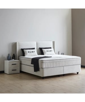 
Ruby Boxspring De Ruby Boxspring van Beddenscout24 biedt een perfecte combinatie van comfort, stijl en praktische opbergruimte. Het bed is verkrijgbaar in 90x200, 140x200, 160x200 en 180x200 cm, waardoor het geschikt is voor elke slaapkamer. Dankzij de ruime opbergruimte onder het matras berg je eenvoudig dekens, kussens of andere spullen op. De opbergruimte is toegankelijk via gasveren en zorgt voor een nette, georganiseerde kamer. Het 7-slags pocketveringmatras van 31 cm dik biedt optimale ondersteuning en comfort. Afgewerkt met koudschuim past het matras zich aan de contouren van je lichaam aan en zorgt het voor drukverlichting. De luxueuze meubelstof bekleding geeft het bed een stijlvolle uitstraling. Het elegante hoofdbord met verticale stiknaden voegt karakter toe aan je slaapkamer. Het is 12 cm breder dan het bed en 119 cm hoog, waardoor het een opvallend maar stijlvol accent vormt. De stevige metalen constructie en luxe stoffering zorgen voor duurzaamheid en jarenlang comfort. Met een instaphoogte van circa 70 cm en poten van 10 cm is de Ruby Boxspring niet alleen comfortabel maar ook praktisch in gebruik. Onderhoud is eenvoudig door regelmatig stofzuigen met een zachte borstel. Optioneel kan het bed professioneel worden gemonteerd. Voeg een topper toe voor extra comfort en geniet van een complete slaapoplossing met de Ruby Boxspring.Specificatiesinclusief Pocketvering Hybride Matras 32 cmMateriaal: StaalKleur: WitAfmetingen: 180x200 cm