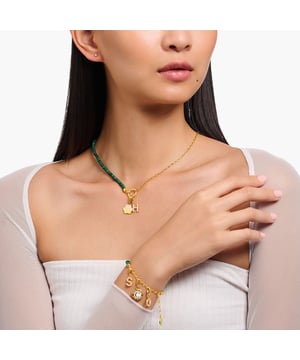 Thomas Sabo Bedelketting met Kralen. Een heerlijke combinatie van een hoogwaardige 925 Sterling zilveren schakel in 18k vergulde ketting met groene malachiet imitatie kralen. De schakelketting is versierd met een ronde THOMAS SABO Charm Club Charmista munt, met de hand beschilderd met sprankelend groen koud email. De kralenketting is voorzien van ingewikkeld ontworpen eindkappen met gegraveerde lijnen. Materiaal: 100% 18k verguld sterling zilver (gerecycled). Ref: KE21901406.