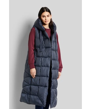 Die lange Weste im asymmetrischen Stil mit Kapuze ist aus einer versteppten sowie recycelten Qualität. Die Jacke lässt sich mit Druckknöpfen verschließen. Details und Innenleben sind edel abgestimmt und setzen dezente Akzente. Für eine ideale Wärmeisolation sorgt die Füllung; die auf nachwachsenden Rohstoffen basierende Faser.