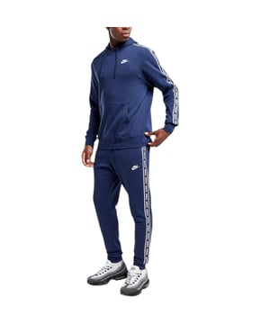 Nike Club Tape GX Suit in Midnight Navy Plush 2-piece suit crafted from high-quality, sustainable and breathable materials. Great for training and active leisure. The top half is an overhead hoodie complete with adjustable drawstring hood, rib cuffs and hem, contrast sleeve branding tape, front kangaroo pouch pocket and Nike logo to left chest. The matching bottoms boast an elasticated adjustable drawstring waistband, rib cuffs, open hand pockets and the same matching contrast side tape