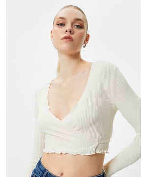 Stijlvolle ecru crop blouse met een V-hals en lange mouwen, perfect voor een modieuze look. Deze blouse is ribgebreid en heeft een omslagontwerp met strikdetail aan de achterkant. Ideaal voor zowel casual als meer formele gelegenheden, en gemakkelijk te combineren met een blazer of hoge taille broek.  Productkenmerken  - Type Mouwen: Lange mouwen - Type Kraag: V-hals - Detail: Binding aan de achterkant - Pasvorm: Slank en ribgebreid - Gebruik: Casual en formele gelegenheden