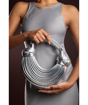 The Blossom Curved Metallic Shoulder Bag is a bold statement piece with a sculpted silhouette that adds instant glamour to any outfit. Crafted from faux leather with a radiant metallic finish, it features a distinctive curved design and structured handle detail that make it stand out from the crowd. Compact yet functional, it offers enough space for evening essentials while remaining lightweight and stylish. Perfect for parties, special occasions, or when you want your accessories to make an impact. Key Features: • Material: Faux leather with metallic finish • Dimensions: Compact curved shape for essentials • Fastening: Secure top closure • Detail: Sculpted curved design with structured handle for statement style