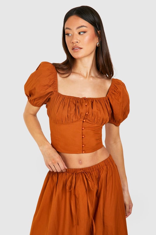Plunging square neckline for a daring look
        Puff sleeves add a romantic touch
        Button-down front detail for adjustable styling
        Cropped length to showcase your midriff
        Fitted waist creates a flattering silhouette
    
    Make a statement in this eye-catching crop top that combines vintage charm with modern flair. The plunging neckline and puff sleeves create a captivating contrast, perfect for those looking to turn heads on a night out. Pair it with the matching high-waisted skirt for a coordinated ensemble that's sure to impress at your next social gathering. For a more casual look, team it with high-waisted jeans and trainers. The versatile design allows for easy transition from day to night - simply swap your footwear and add some bold jewellery to elevate your outfit for evening drinks or dancing. This Boohoo piece is ideal for the fashion-forward woman who isn't afraid to showcase her style and confidence.