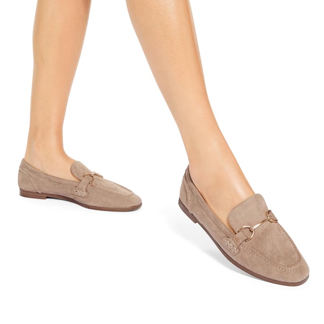 The KG Kurt Geiger Madeline is a taupe microsuede slip on loafer. There is an antiqued brass horse bit chain across the toe and small KG Kurt Geiger stud.