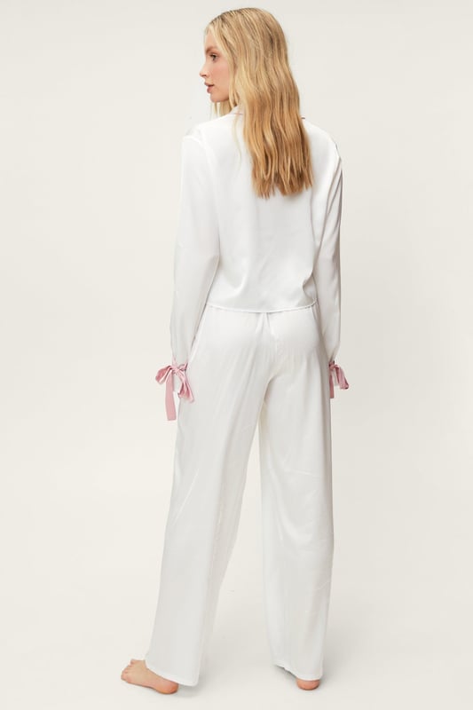 Early nights pending. Feel luxe in our pajama pants set, with button fastenings, an ultra comfortable relaxed fit, and ruffle trims. Style them with slippers and a robe for a look that will take you from movie nights to lazy mornings. Satin Contrast Piping Tie Sleeve Pajama Pants Set Feminine Ruffle Design Unique Tie Sleeve Details Flattering Relaxed Fit Button Up Pajama Shirt Comfortable High Waist Pajama Pants Model wears a size M (US size 6/UK size 10).
