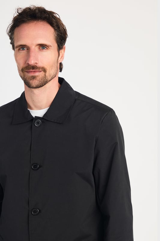 This men's mac-style coat from Kensington Eastside features a classic collar, button-up fastening, and a mid-length cut for a sleek, modern look. Lightweight and stylish, it’s perfect for layering over both casual and formal outfits, making it a versatile wardrobe essential for effortless style.