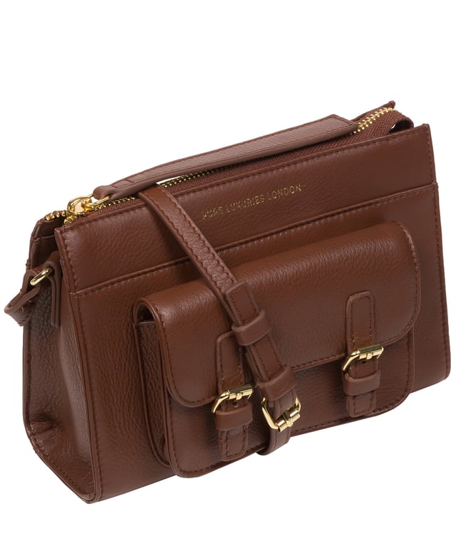 Handcrafted from Nappa leather, the 'Monica' cross body bag from the Pure Luxuries London Marylebone Collection elevates this classic design. A spacious main compartment is secured under a zip-over top which is lined with 100% cotton for a luxurious feel. Two slip pockets on the interior of the bag provide additional storage space - ideal for maintaining an organised accessory. Complementing the interior storage is a stylish pocket secured with a press-stud fastener made to look like a buckle reminscent of the classic satchel design. Gold-coloured metal fittings and zips adorn the bag alongside the slim and adjustable leather strap with a maximum drop length of 65cm. The Pure Luxuries logo is embossed in gold foil for a beautifully simple finishing touch.