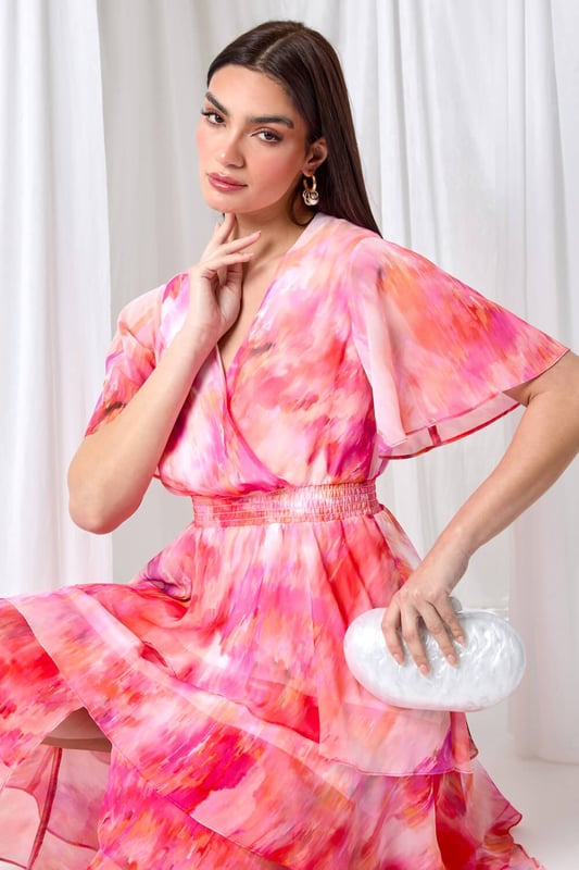 Abstract Print Chiffon Tiered Midi Dress from Roman. Discover pure elegance with this abstract print tiered midi dress from the Ariella collection. This wedding guest staple features a soft chiffon fabric with a flattering tiered silhouette and a v-neckline. Designed with a wrap front and shirred stretch waist for a fit and flare shape, this will be flattering for any formal event. The vibrant abstract print, split detail skirt, and short floaty sleeves add a touch of femininity to the finished look. Whether you're ready for a day at the races or you're Mother of the Bride, this dress is easy to pull on overhead and style with heels for timeless occasionwear.