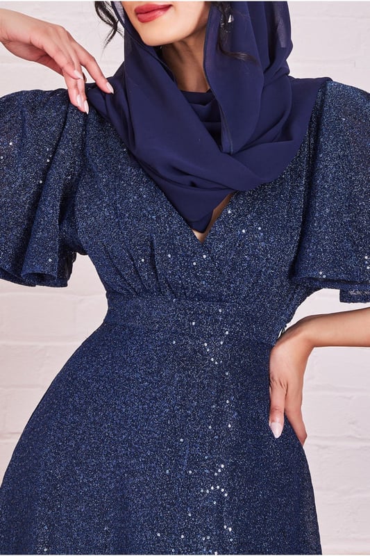 *PLEASE NOTE SCARF IS NOT INCLUDED*The Sequin Lurex Flutter Sleeve Maxi Dress from Goddiva is the dress for you! This dress is perfect for any occasion, from daytime events to evening soirees, and is ideal for bridesmaids or mothers of the bride (or groom). With its wrap style v-neckline and flutter sleeves, this dress has a feminine and elegant touch. The a-line skirt complements the flutter sleeves perfectly, creating a silhouette that is both flattering and modest. The sequin and lurex finish adds an extra touch of glamour and sparkle to this navy dress, making it perfect for any formal event. This dress is also a great choice for modest fashion, making it perfect for Eid celebrations or other events where modest dress is preferred. The striking and sparkly effect of the sequins and lurex fabric creates a bold yet elegant look that is sure to turn heads. Pair this maxi dress with a scarf, strappy sandals and a statement necklace to complete the look.