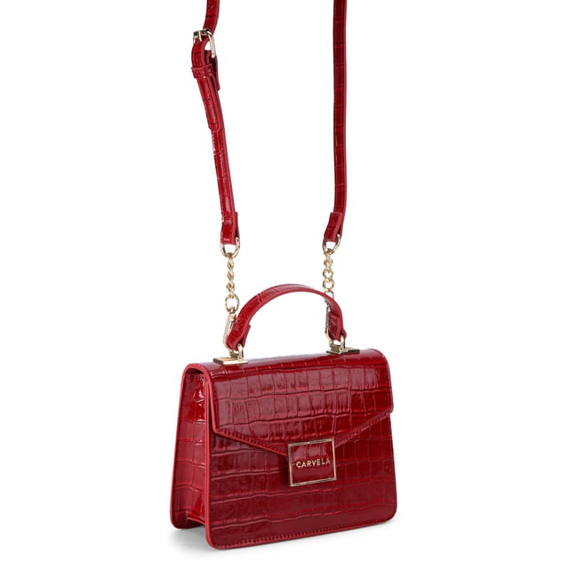 This Carvela Jessica Top Handle Bag features a deep red exterior with large croc print. There is a gold branded plate on the front flap. Dimensions: 15cm (H), 17cm (L), 7cm (D). Strap length: 125cm.