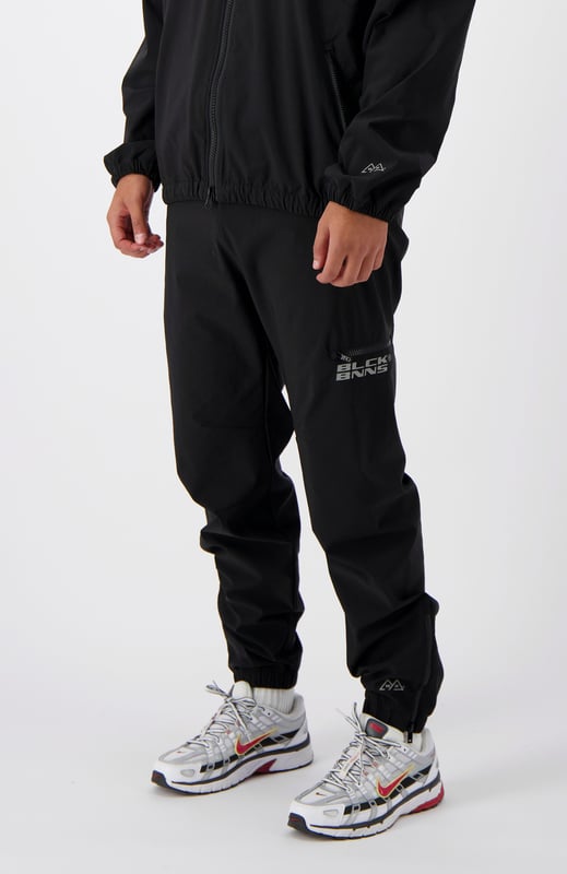 90 % Nylon | 10 % Elastan Elastischer Bund Schwarzes BNNS-Logo auf dem linken Bein Zwei Reißverschluss-Fronttaschen Kombinierbar mit INITIAL TECH JACKET 