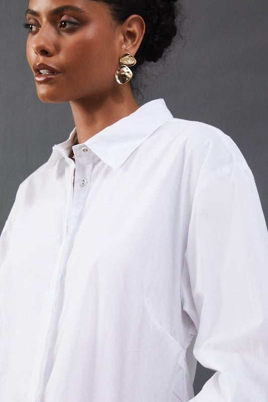 Striking open back design with tie detail
        Classic collared neckline for a polished look
        Long sleeves with button cuffs for versatility
        Relaxed fit through the body for comfort
        Crafted from breathable cotton poplin fabric
    
    Make a statement with this eye-catching poplin shirt from Warehouse. The open back design with delicate tie detail adds an unexpected twist to a classic silhouette, perfect for those who want to inject a bit of edge into their wardrobe. The relaxed fit and breathable cotton fabric ensure all-day comfort, while the collared neckline maintains a smart appearance. Style this versatile piece with your favourite denim for a casual daytime look, or dress it up with tailored trousers for a chic ensemble suitable for family gatherings or brunch with friends. The long sleeves can be rolled up for a more relaxed vibe, making this shirt adaptable for various occasions. Pair with flat sandals or trainers to complete your effortlessly cool outfit.