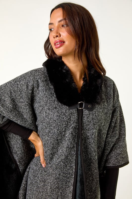 Faux Fur Fringe Hem Poncho from Roman. This style is ONE size.  Wrap up in style with this chic fringe detail poncho. Featuring a luxurious fur trim collar for added elegance and a trendy fringe hem for a playful finish, this poncho is the perfect layering piece for the Autumn/Winter season. Throw it on over your favourite knitwear and jeans for a fashion-forward look that will keep you both warm and stylish throughout the colder months!