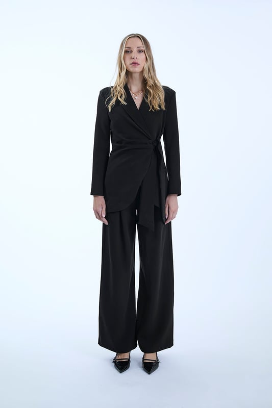 Chic James Lakeland Blazer with a shawl lapel and glamorous front ruching. Features a hidden front button and long sash belts for tying. Curved hems create a cinched waist illusion. Three-quarter sleeves and slim silhouette tailoring make this a sleek, stylish piece.