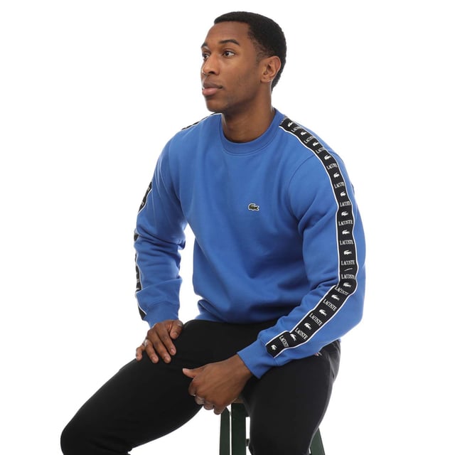 Mens Lacoste Logo Stripe Jogger Sweatshirt in blue.- Ribbed crewneck.- Elasticated cuffs and hem.- Embroidered logo on the chest and a logo pattern down both sleeves.- Classic fit.- Shell Fabric: 80% Cotton  20% Polyester. Rib edge: 98% Cotton  2% Elastane.- Ref: SH749200IXV