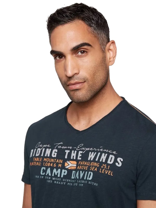 Dieses Herren-T-Shirt vereint lässigen Stil mit raffinierter Detailverliebtheit. Der V-Ausschnitt mit Used-Kante verleiht dem Shirt einen coolen, entspannten Look. Die Flammgarnstruktur sorgt für eine einzigartige Textur und unterstreicht die Individualität des Designs. Kontrastnähte an den Schultern setzen subtile Akzente, die das Gesamtbild perfekt abrunden. Ein markanter Front-Print mit Flockprint-Details zieht alle Blicke auf sich, während ein kleiner Logo-Print hinten und ein Label-Patch am linken Ärmel dezente Markenakzente setzen. Das Necktape sorgt für zusätzlichen Tragekomfort und Stabilität. Mit seiner normalen Passform und dem hohen Tragekomfort ist dieses Shirt ein Must-have für jeden Kleiderschrank. Ideal für lässige Outfits, die dennoch Stilbewusstsein ausstrahlen. Ein zeitloses Stück, das in keiner Garderobe fehlen sollte.