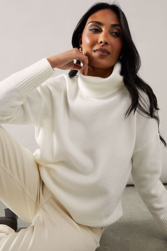Asymmetric hemline for a modern, eye-catching silhouette
        Cosy roll neck design perfect for chilly days
        Relaxed fit through the body for effortless comfort
        Long sleeves with ribbed cuffs for a snug fit
        Versatile knit suitable for various casual occasions
    
    Embrace sophistication and comfort with this Wallis Petite Plain Asymmetric Roll Neck Jumper. The unique asymmetric hemline adds a contemporary twist to this classic knitwear piece, making it a standout addition to your wardrobe. Perfect for those who appreciate both style and cosiness, this jumper is ideal for family gatherings, casual outings, or relaxed evenings with friends. Style it with dark wash jeans and ankle boots for a chic daytime look, or pair it with tailored trousers and ballet flats for a more polished ensemble. The versatile design allows for easy transition from day to night, ensuring you always look put-together without compromising on comfort. Add delicate gold jewellery to enhance the jumper's elegant appeal, making it a go-to piece for those moments when you want to feel both glamorous and at ease.