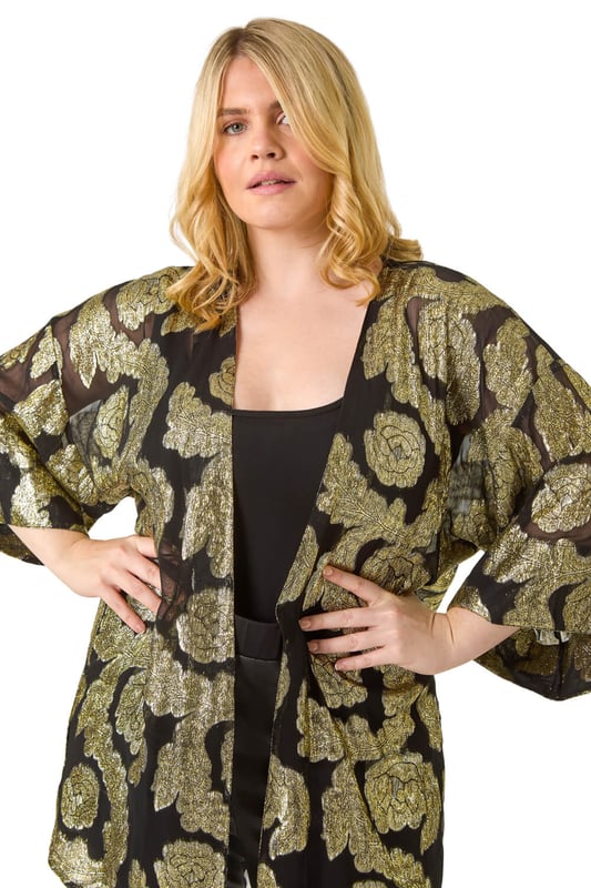 Curve Floral Foil Print Kimono from Roman. Be the star of the show at your next event with our glamorous Curve foil kimono. The woven fabric is adorned with floral foil print for a sparkling finish, perfect for special occasions. The classy edge-to-edge opening and 3/4 length sleeves add a sophisticated touch, while this kimono finishes around knee-length. Pair this kimono with wide-leg trousers and heeled boots for a stylish outfit that will turn heads wherever you go!