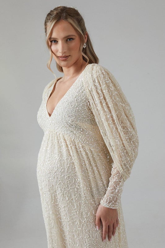 Exquisite hand-stitched embellishments for a luxurious finish
        Elegant V-neckline complemented by long sleeves
        Stunning cowl back detail for added sophistication
        Floor-length design with a graceful silhouette
        Maternity-friendly cut to accommodate and flatter your changing shape
    
    Radiate bridal elegance in this captivating maternity wedding dress from Coast. The hand-stitched embellishments create a dazzling effect, perfect for catching the light as you walk down the aisle. The V-neckline and long sleeves offer a timeless appeal, while the cowl back adds a touch of drama to your ensemble. Designed with the expectant bride in mind, this gown gracefully accommodates your changing silhouette, ensuring comfort throughout your special day. Style with delicate drop earrings and a simple bracelet to let the dress take centre stage. For a complete bridal look, consider a floor-length veil and ivory satin heels. This gown is not just for the ceremony; it transitions beautifully to the reception, allowing you to dance the night away in style and comfort.