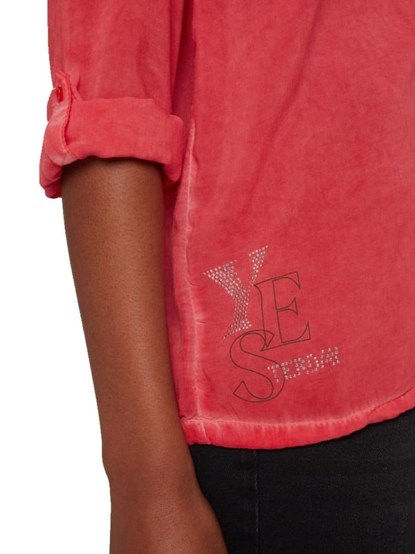 Deze blouse met borstzak voor dames is een veelzijdig basisstuk. De tuniekhals eindigt in een doorlopende knoopsluiting. In de zoom zit een trekkoord waarmee de wijdte naar wens kan worden aangepast. De lange mouwen hebben manchetten met knopen en knoopsluitingen aan de binnenkant, zodat de mouwen kunnen worden opgerold en vastgezet. De speciale olieverf geeft de blouse een heel bijzondere uitstraling. De grote labelversiering op de rug en de twee kleinere prints op de borstzak en boven de zoom zijn afgewerkt met glittersteentjes.