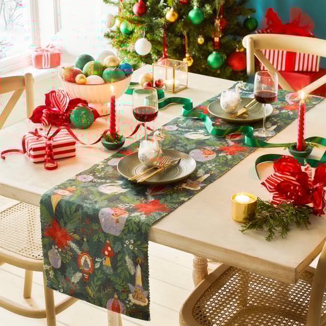 Get into the Christmas spirit with this wonderfully festive table runner. Featuring a digital printed design on woven polyester fabric of Christmas foliage and traditional tree decorations, including vintage baubles, candles and even a swan in vivid seasonal colours. This beautiful table runner will transform and add some instant seasonal cheer to your Christmas dining table.