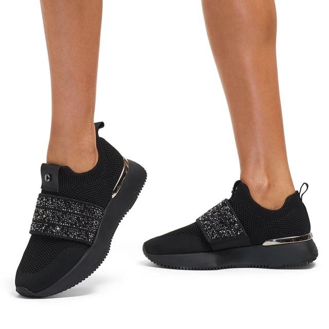 The Carvela Flare Sparkle trainer is a slip-on style with a black knitted upper. There is a crystal encrusted black fabric strap across the foot. The sole is chunky in black.