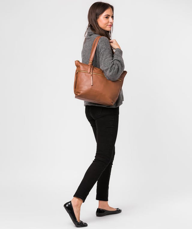 The 'Moorgate' tote bag from Cultured London is both practical and smart, crafted from premium nappa leather that is soft to the touch and adorned with gold metal fittings. The spacious compartment comes with two slip pockets, lined with natural 100% cotton and is secured by a zip-over top. An additional zipped pocket on the front and a slip pocket on the rear provide on-the-go storage. Comes with adjustable leather handles and is adorned with a gold foil embossed Cultured London logo and charm.