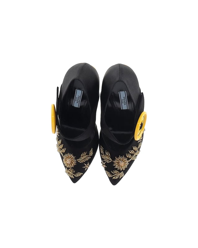VINTAGE, UVP WIE NEU  
Diese atemberaubenden Pumps spiegeln Pradas exquisite Handwerkskunst im Schuhbereich wider. Hergestellt aus glattem Satin in einem schwarzen Farbton, verfügen sie über filigrane Verzierungen auf dem Obermaterial, einen Riemen im V-förmigen Design, der mit übergroßen gelben Knöpfen befestigt ist, und schlanke, spitze Zehen. Charakteristisch für die Pumps sind die atemberaubenden mit Kristallen besetzten Absätze in Gold-Optik.  

Prada Verzierte Gold- und Kristallabsatzpumps aus schwarzem Satin  
Zustand: sehr gut  
Material: Satin  
Größe: EU37  
Tragespuren: leichte Abnutzung an der Sohle  
SKU: 360962