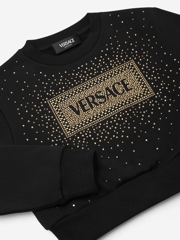 Versace envision bold, innovative abstracts in their beautifully crafted aesthetics. This girls black cropped sweatshirt encapsulates the Italian label's passion for daring and unparalleled technology. Envisioned in soft cotton jersey with a 90s-inspired vintage Versace logo embellished with crystals and studs on the front.  Made in Italy Brushed Cotton Long Sleeves Ribbed Crew Neck, Cuffs and Hem 100% Cotton