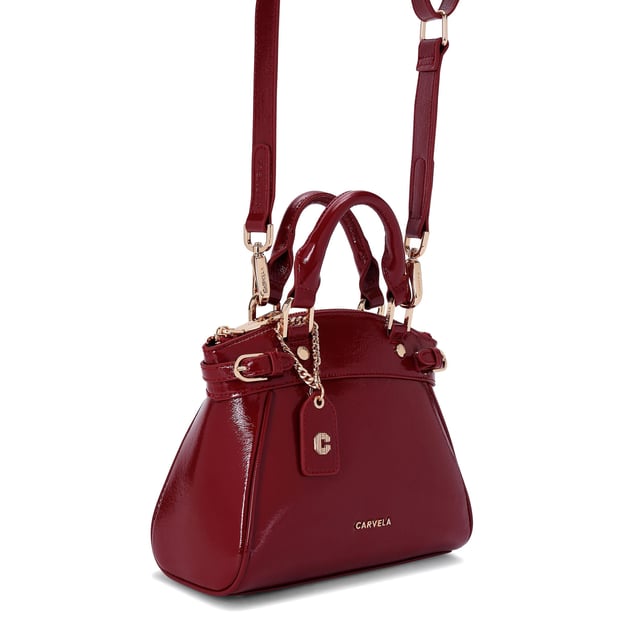 This Carvela Mini Valentina Tote bag features a wine red exterior in a trapeze style. There are two buckled straps across each side of the bag and branded gold tone hardware across the bag. Dimensions: 19cm (H), 22cm (L), 10cm (D). Strap length: 111cm.