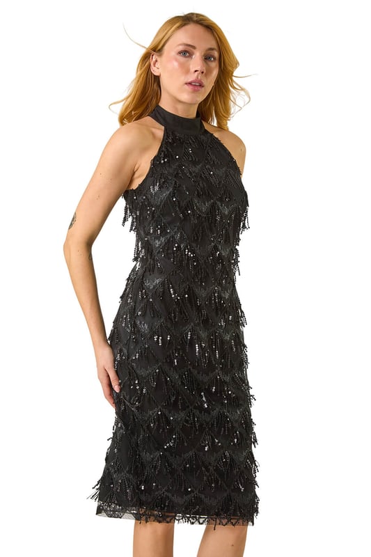 Tassle Trapeze Dress from Roman. Add a touch of glamour to your wardrobe with our halter neck trapeze dress. Showcasing a feminine halter neckline and sleeveless style, this dress boasts an elegant bodycon shape adorned with embellished details and a stunning tassel design. Crafted from a comfortable woven fabric, this dress is perfect for all-day wear. Finish this look above knee length with heels and a bolero for a special occasion!