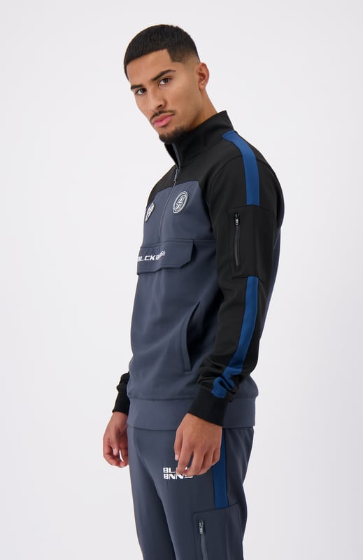 100 % poliéster Cuello alto con media cremallera Camino de convoy en el pecho Bolsillo lateral con cremallera en el brazo izquierdo Solapa distintiva de BNNS en color negro Dos bolsillos delanteros con cremallera Mangas a rayas Se puede combinar con RUMBLE TRACKPANTS